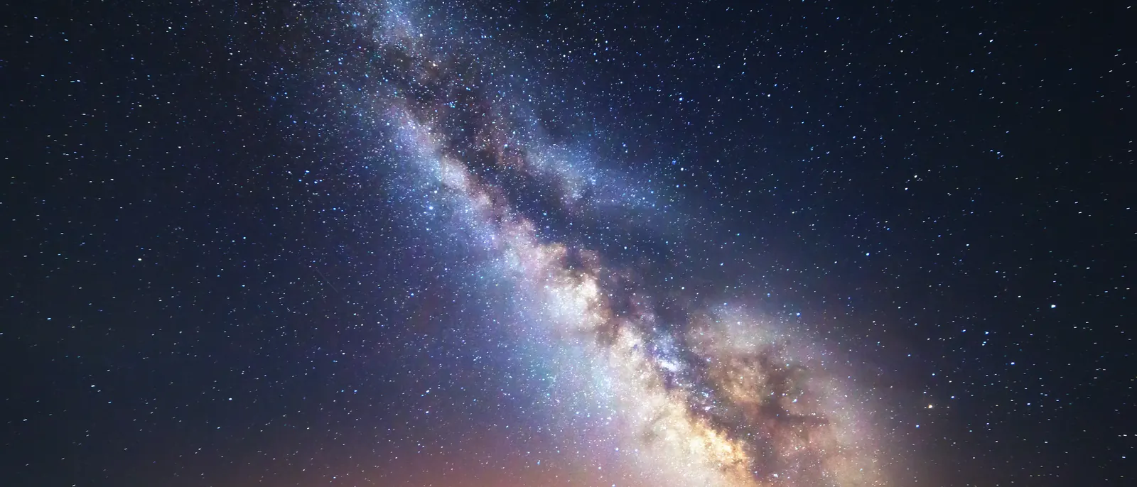 The Milky Way over a dark ridge, with a faint glow on the horizon.