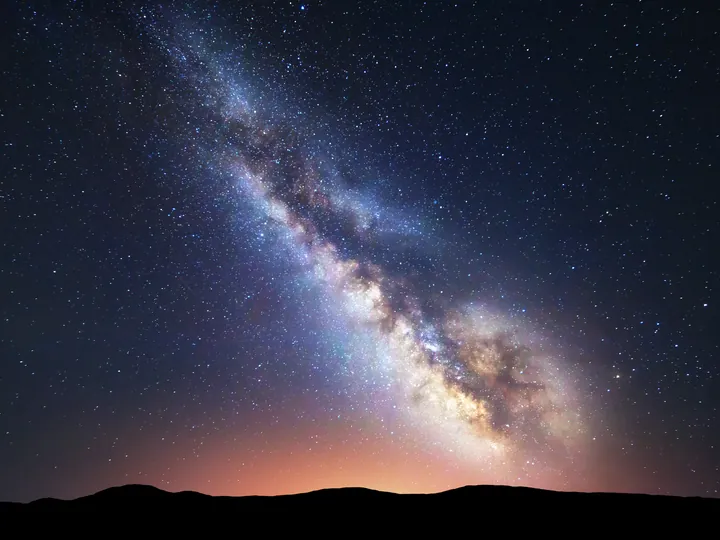 The Milky Way over a dark ridge, with a faint glow on the horizon.