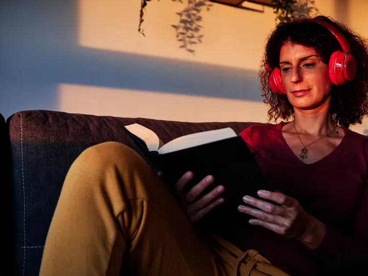 Someone reading a book in headphones by lamplight.