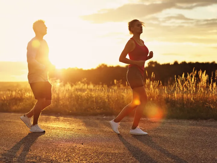 Two runners on a country road, backlit by a low sun.
