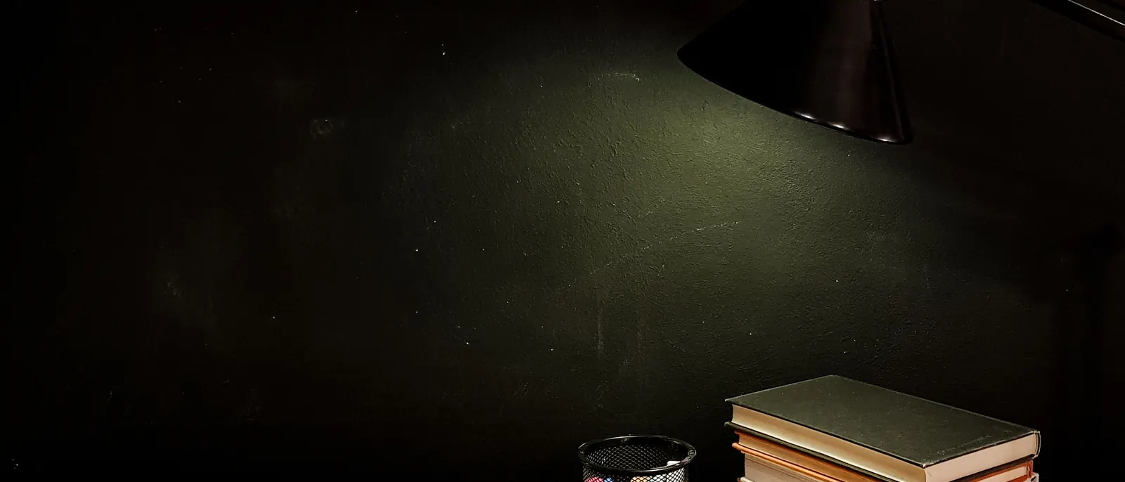 Books and a lamp on a wooden table at night.