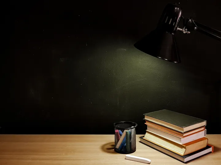 Books and a lamp on a wooden table at night.