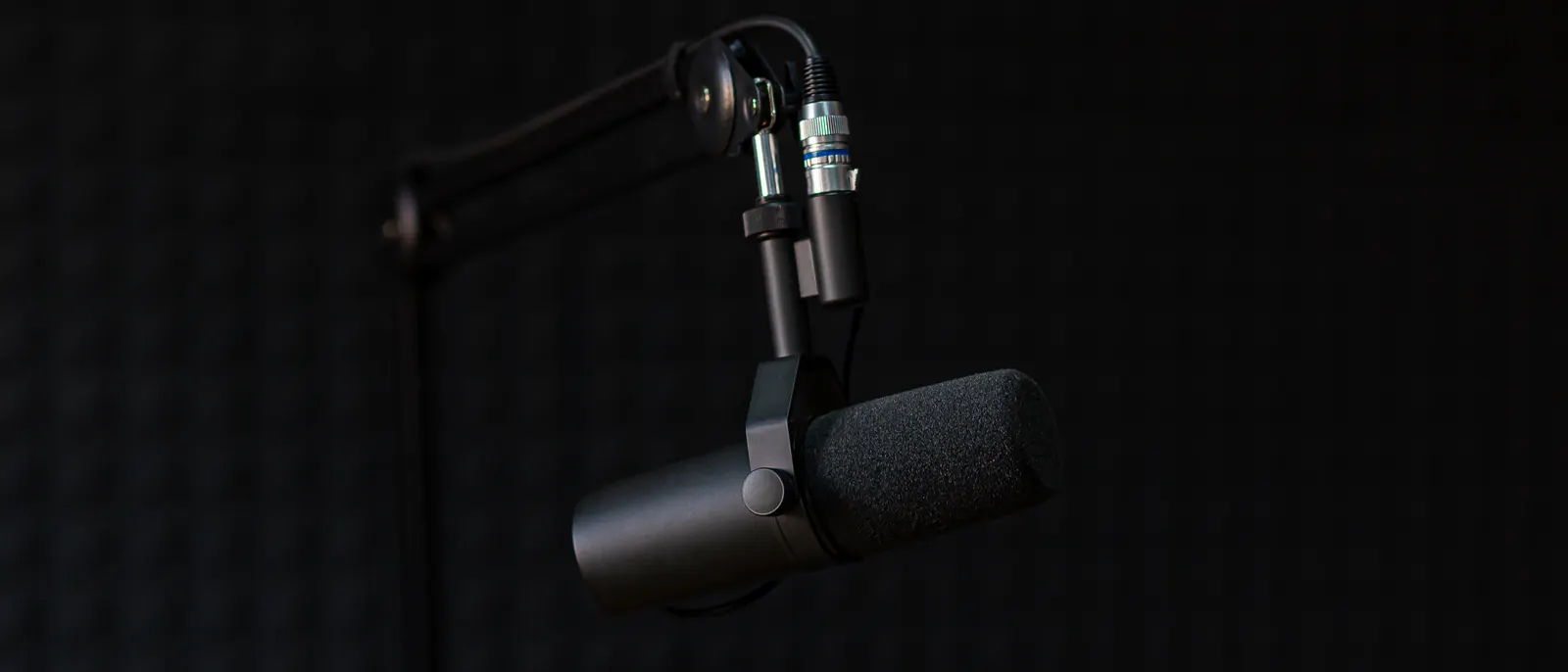 A broadcast microphone on a boom arm against a black wall.