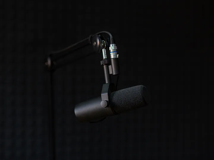 A broadcast microphone on a boom arm against a black wall.