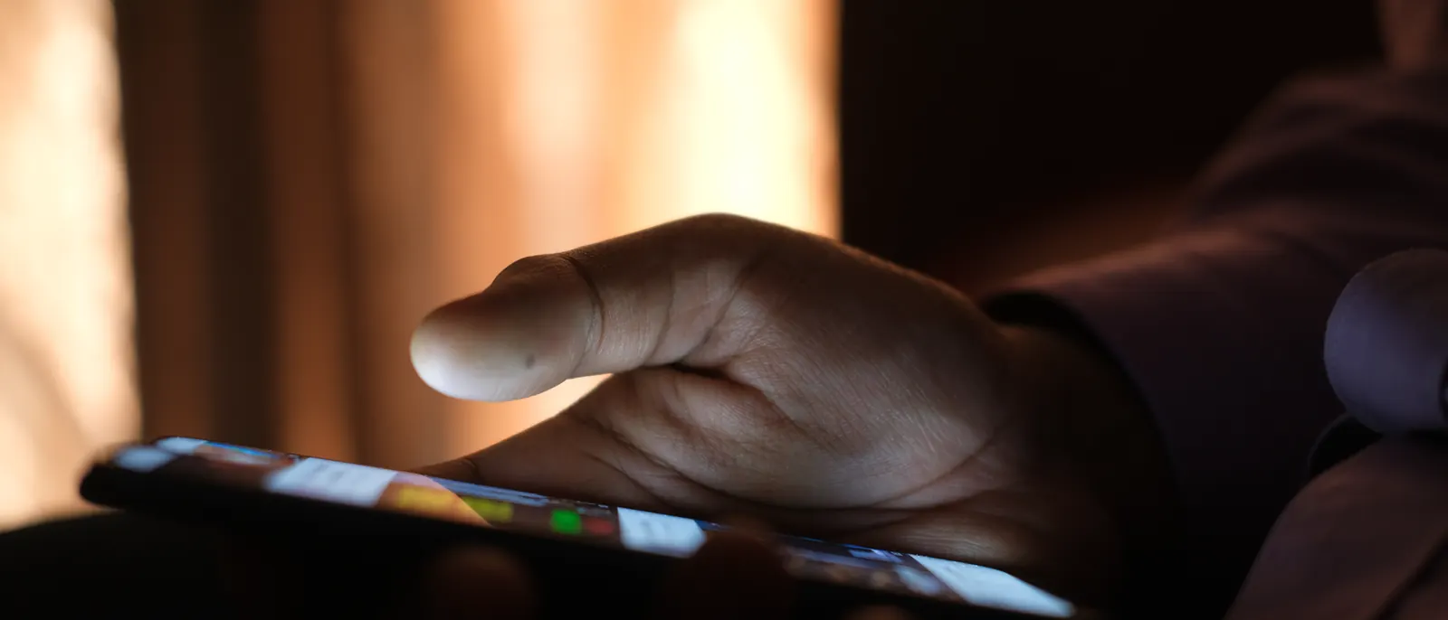 A hand holding a lit phone screen in a dark room.