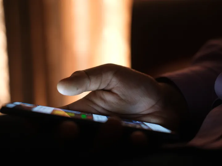 A hand holding a lit phone screen in a dark room.