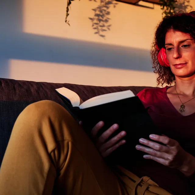 Someone reading in headphones on a sofa in late daylight.