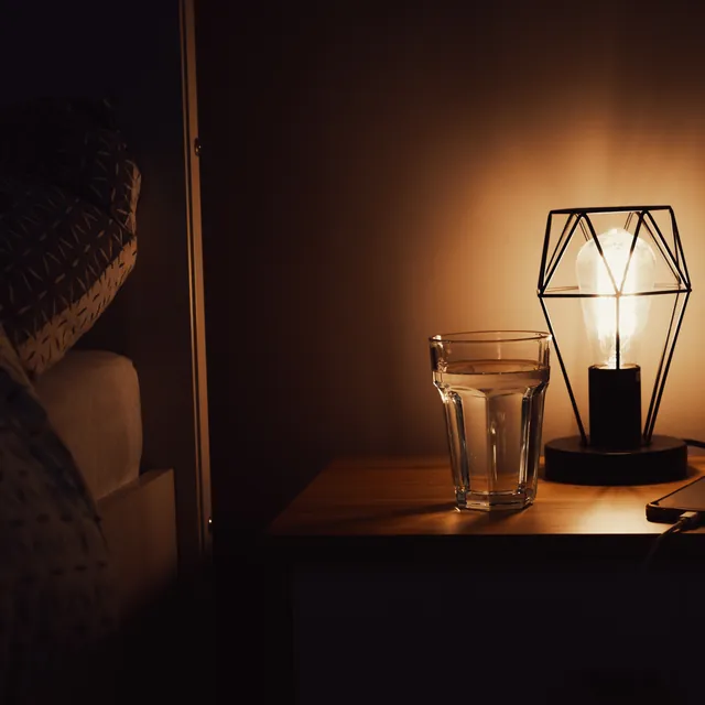 A bedside lamp, a glass of water and a phone face down on a table.