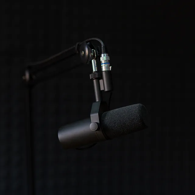 A broadcast microphone on a boom arm against a black wall.
