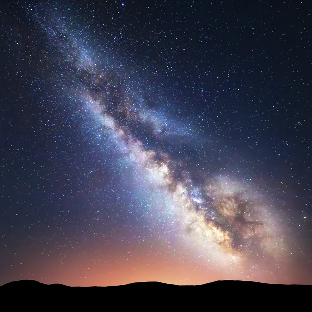 A star-filled night sky above a dark ridge.
