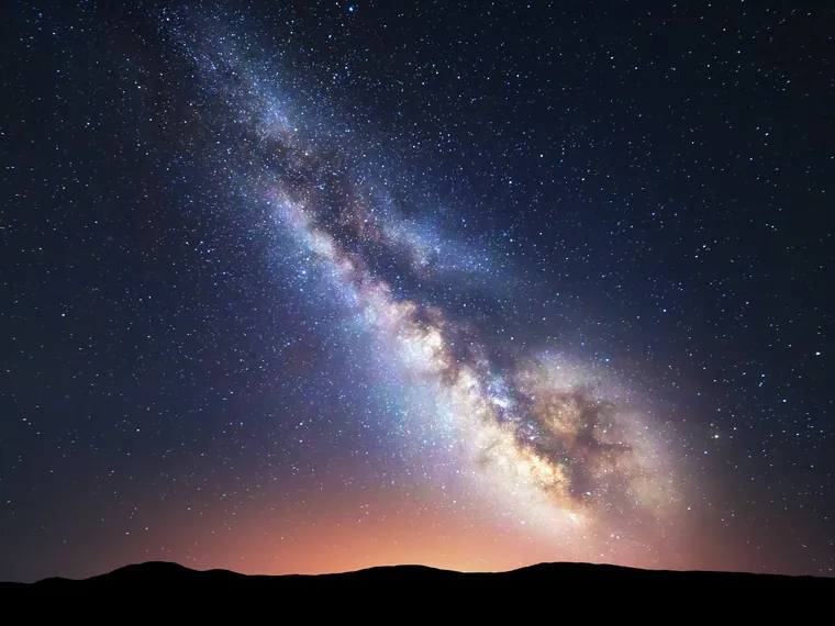 The Milky Way over a dark ridge, with a faint glow on the horizon.